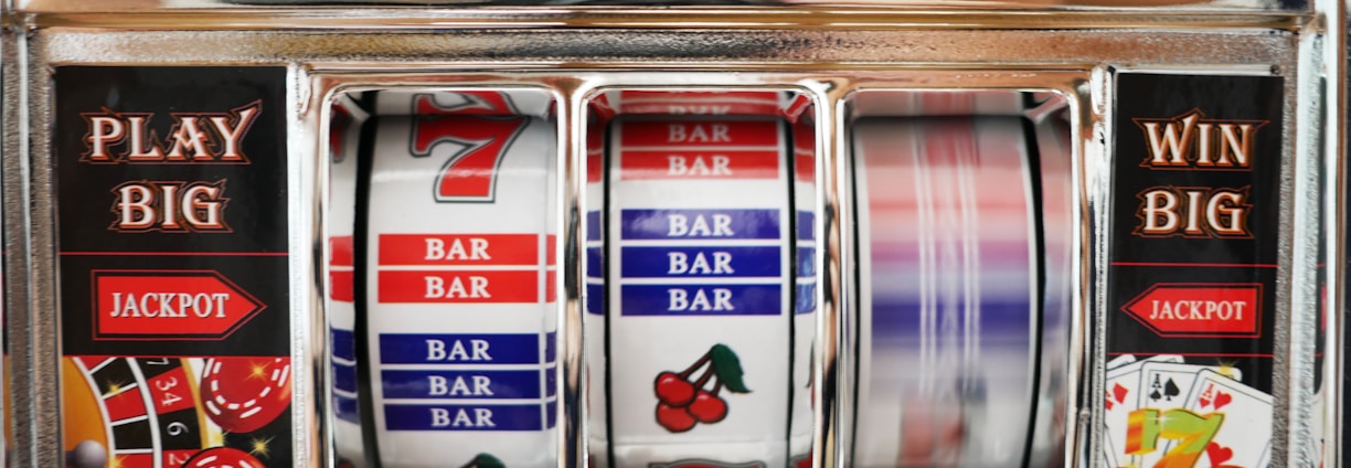 A close-up view of a slot machine with vibrant colors and various gambling symbols such as dice, coins, and playing cards. The reels display a combination of symbols, including bars, cherries, and the number seven. The chrome exterior and colorful details convey the theme of casino and gambling.